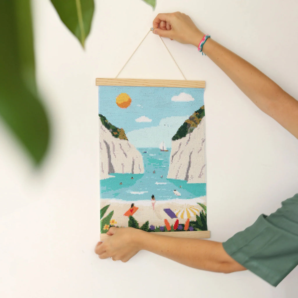 Toile « Petit Diamond – Kit Diamond Painting Stiniva Beach » finie en train d'être installée dans une pièce.